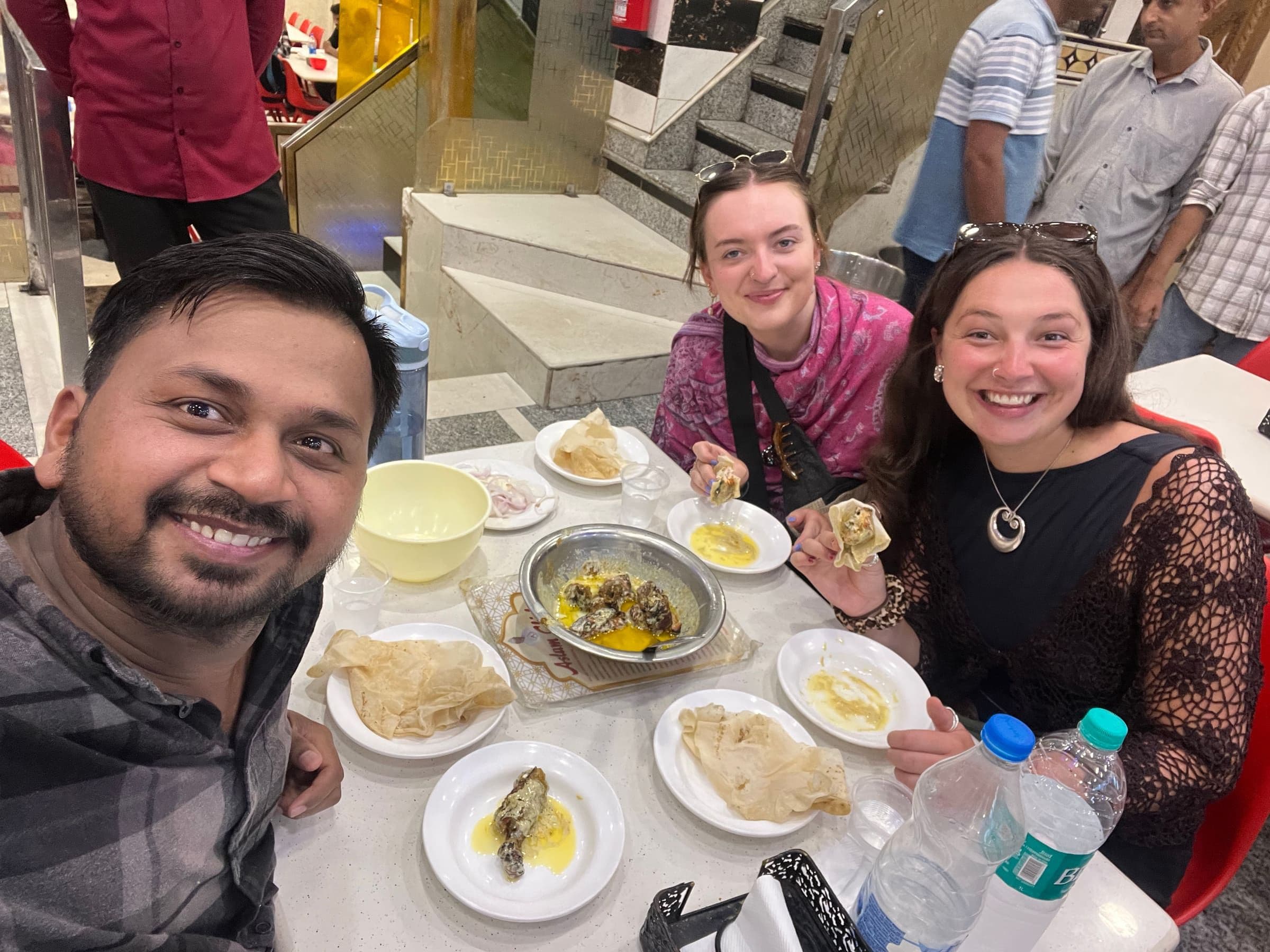 Guide and guests smiling over a table full of street food on the Old Delhi Food Tour